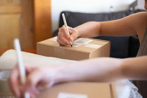 Hands labelling a cardboard shipping box with a marker