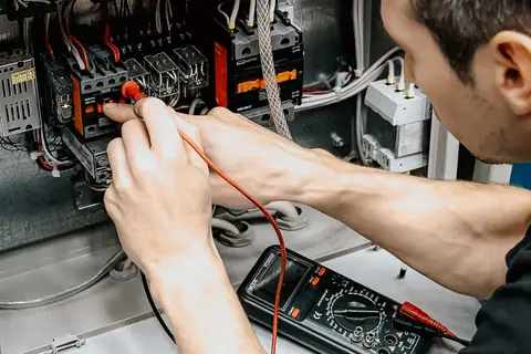Electrician testing wiring in an open switchboard with a multimeter