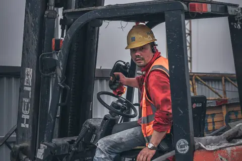 Forklift driver in a hard hat and hi-vis at work in a yard
