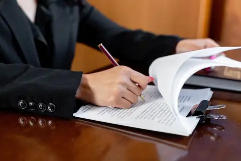 Close-up of a person reading and signing paperwork at a desk
