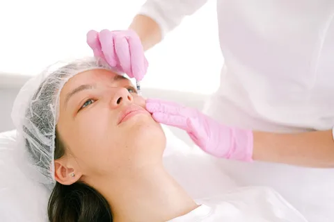 Clinician in pink gloves giving a cosmetic injection to a client’s face