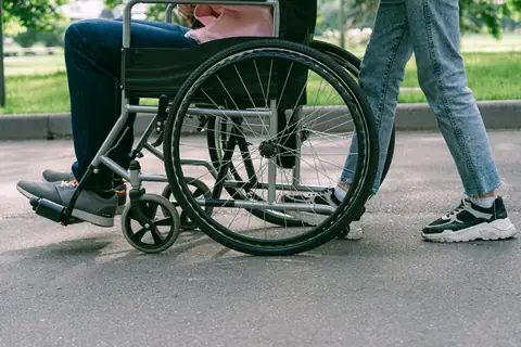 Support worker walking beside a person in a wheelchair on a sunny footpath