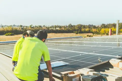Two installers in hi-vis kneeling beside rows of solar panels on a sunny rooftop