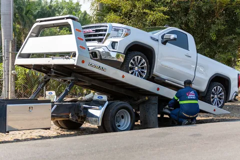 Tow truck operator loading a white ute onto a tilt tray
